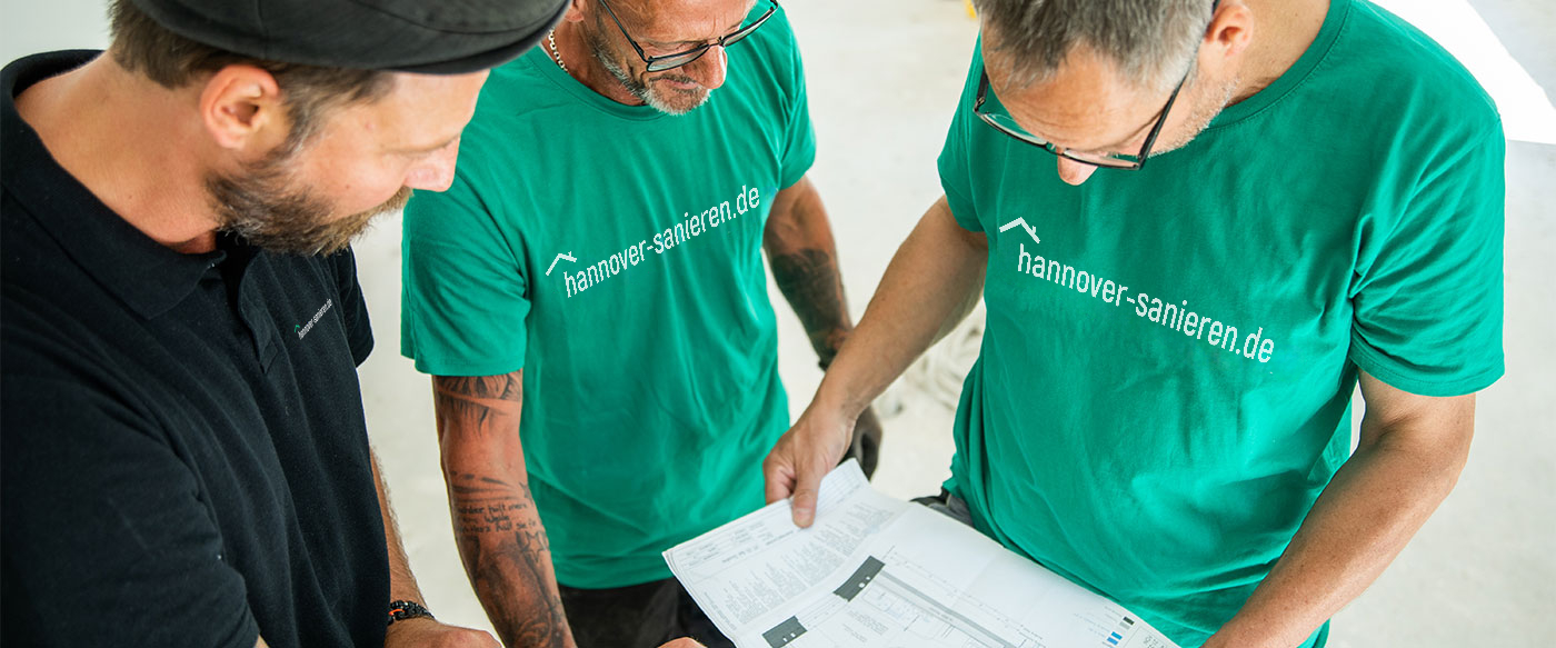 Drei Bauprofis von hannover-sanieren.de besprechen Baupläne auf einer Baustelle, mit Fokus auf professionelle Sanierungsplanung.